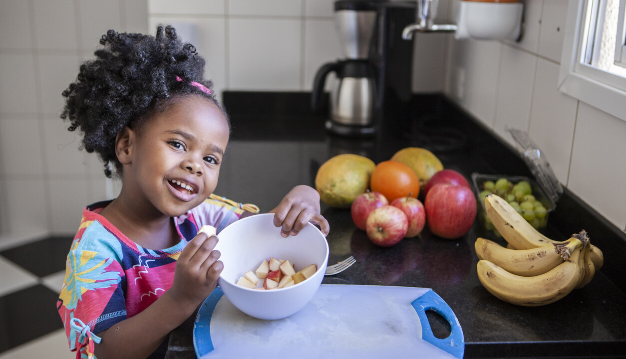 A little girl eating a bowl of fruit.