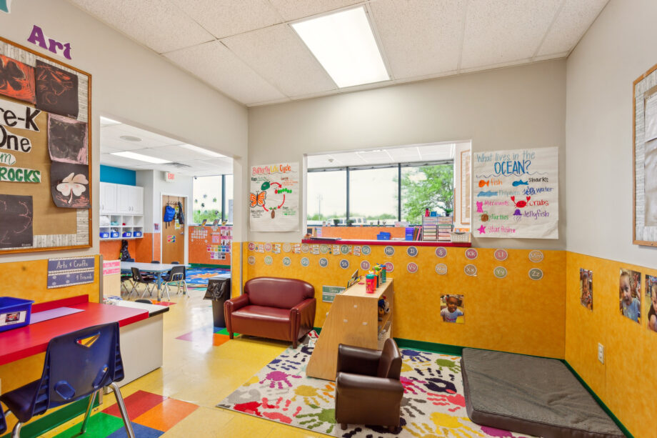 Colorful preschool classroom with small tables, chairs, armchairs, educational posters on the walls, and toys neatly arranged; large window lets in natural light.