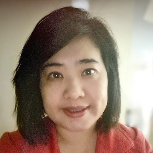 A woman with straight, dark hair and wearing a red top looks toward the camera and smiles slightly. The background is softly blurred.