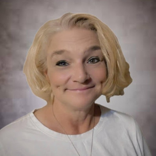 A woman with short blonde hair wearing a white shirt, smiling softly at the camera with a neutral, blurred background.
